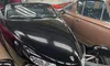 A sleek black retro-styled sports car is parked among several vintage vehicles in a showroom lined with hubcaps on the walls.