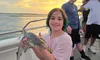 A smiling child on a boat holds a small shark against a backdrop of a scenic sunset.