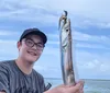 A smiling man and woman are posing on a boat with a freshly caught fish, with fishing rods and the water visible in the background.