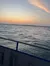 A tranquil sunset view over the ocean, seen from a boat with railings in the foreground.