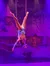 A trapeze artist is performing an aerial act against a snowy village backdrop.