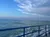 A view of the ocean with gentle waves and partly cloudy skies, taken from a vessel with a blue railing.