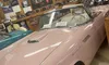A vintage pink Thunderbird convertible is displayed in a room decorated with automotive memorabilia and signage.