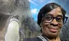 A woman wearing glasses takes a selfie in front of a penguin exhibit.