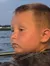 A young child gazes thoughtfully into the distance over a body of water from the side of a boat at dusk.
