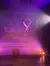 An acrobat is performing an aerial hoop act on stage with a snowy village backdrop illuminated by colorful stage lights.
