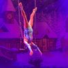 An acrobat performs an aerial act on a trapeze against a snowy village backdrop.