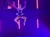 An aerial performer is suspended in mid-air on a vividly lit stage, surrounded by a backdrop of stars and subtle fireworks.