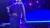 An elderly person with gray hair and a plaid shirt is standing on stage, illuminated by colorful stage lights.