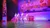 Four performers in sparkling costumes are dancing on stage with a backdrop illustrating a whimsical winter village scene.