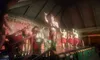 Performers are energetically engaging in a traditional dance on stage, with some wearing grass skirts and tropical attire, evoking a Polynesian cultural performance.
