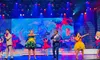 Performers are singing and dancing on a brightly lit stage with colorful costumes and a vibrant digital backdrop.