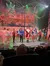 Performers dressed in festive costumes, including a Santa Claus, take a bow on stage in front of a winter-themed backdrop.