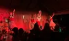 Performers in traditional attire are dancing on stage in front of an audience, illuminated by red lighting.