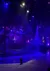 The image captures a dramatic aerial performance with acrobats suspended on ropes or silks, bathed in moody blue and purple stage lighting that creates an ethereal atmosphere.