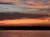 The image captures a dramatic sunset with vibrant orange and pink clouds over a calm body of water and a silhouetted shoreline.