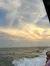The image captures a serene ocean view at dusk with people enjoying the scenery, as seen from a boat, under a sky painted with soft golden hues.