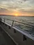 The image captures a serene sunset over a body of water viewed from the side of a boat with metal rod holders lining the rail.