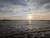 The image captures a serene sunset over a body of water, with sunlight reflecting on the waves and a railing in the foreground.