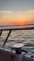 The image captures a serene sunset over the ocean, viewed from a boat's railing.