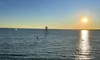 The image captures a serene sunset over the ocean with a clear sky and a silhouette of a navigation marker in the distance.