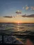 The image captures a serene sunset over the ocean, with gentle waves and a partly cloudy sky.