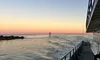 The image captures a serene sunset view from the side of a boat with calm ocean waters and a navigational marker on the horizon.