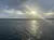 The image captures a serene view of a body of water with ripples, under a partly cloudy sky as the sun sets on the horizon.