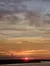 The image captures a tranquil scene of a vibrant sunset over a body of water with silhouetted land on the horizon and clouds streaking across the sky.