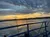 The image captures a vibrant sunset with a mix of orange and blue hues, viewed from the deck of a boat, highlighting the beauty of the sky reflected on the water's surface.