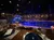 The image depicts an indoor themed dining area with a large pirate ship stage set, surrounded by water and seating areas under dramatic blue lighting.