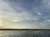 The image features a tranquil waterscape under a vast sky with scattered clouds, taken during the day.