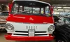 The image shows a classic red and white Dodge vehicle displayed indoors, surrounded by other vintage cars and automotive memorabilia.