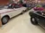The image shows a collection of classic cars displayed in a showroom, with various models including a white car with red stripes and a black Camaro SS.