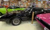 The image shows a collection of colorful classic cars in a garage adorned with vintage memorabilia and license plates.
