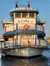 The image shows a paddle steamer boat with a classic design, featuring multiple decks, decorative railings, and a traditional paddlewheel at the back, docked on a calm waterway.