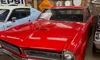 The image shows a red 1965 GTO car on display at 