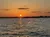 The image shows a serene sunset over a body of water with a clear sky and a few scattered clouds.