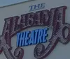 Two people are sitting in a mostly empty theater, smiling at the camera.