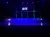The image shows a stage with purple and blue lighting and a large display reading 