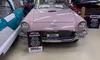 The image shows a vintage 1957 Ford Thunderbird in a museum setting, surrounded by automotive memorabilia and other classic cars.