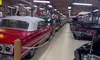 The image shows a vintage car museum with rows of classic cars displayed under a wooden ceiling adorned with model planes and neon signs.