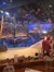 The image shows an indoor theatrical pirate-themed dinner show arena with a water stage, audience seating, and dim lighting adorned with skull decorations.