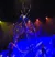 The image shows performers on stage with a large, intricate metal structure and colorful lighting, creating a dynamic and theatrical atmosphere.