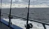 The image shows several fishing rods lined up on the side of a boat with a cloudy sky above and choppy sea waters, possibly indicating a fishing trip in progress.
