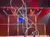 Two acrobats perform on a large rotating metal structure on a brightly lit stage.