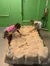 Two children are engaged in a simulated fossil dig activity in an indoor setting with educational or recreational purposes.