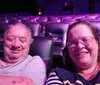 Two people are sitting in a mostly empty theater, smiling at the camera.