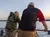 Two people are standing by a railing, looking out over the water during sunset.