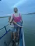 Two people are standing close together on a boat, looking out toward a waterfront with houses under a cloudy sky.